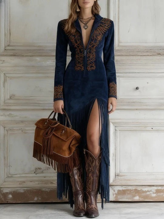 Woman in a dark blue dress with fringe details holding a brown leather bag, standing against a white paneled wall.