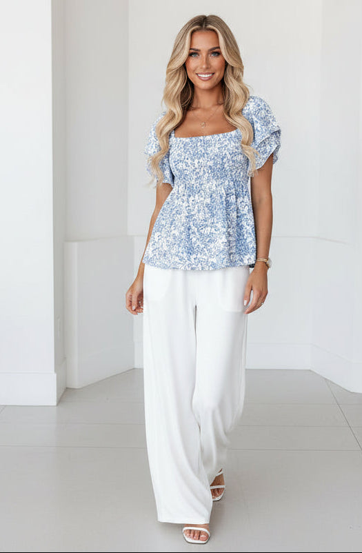 Woman wearing a blue floral top and denim shorts on a neutral background