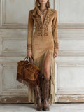 Woman in a long, embroidered brown dress with fringe holding a matching brown bag against a white wall.