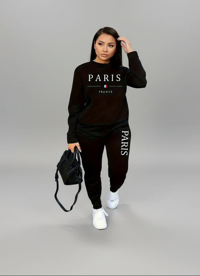 A woman wearing a black sweatsuit set with 'PARIS' printed on the front, paired with white sneakers 