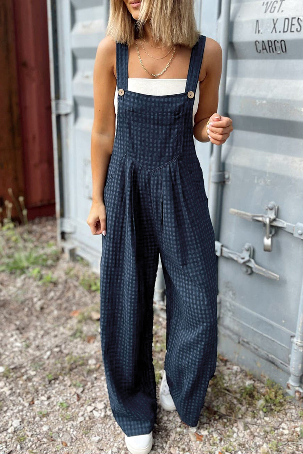 A person wearing a navy blue plaid print jumpsuit with wide-leg pants, buttoned front, and a high waist silhouette