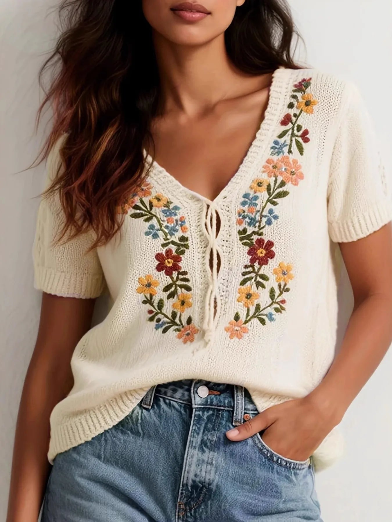 Woman wearing a short sleeve cream-colored openwork pullover knit top with floral embroidery 