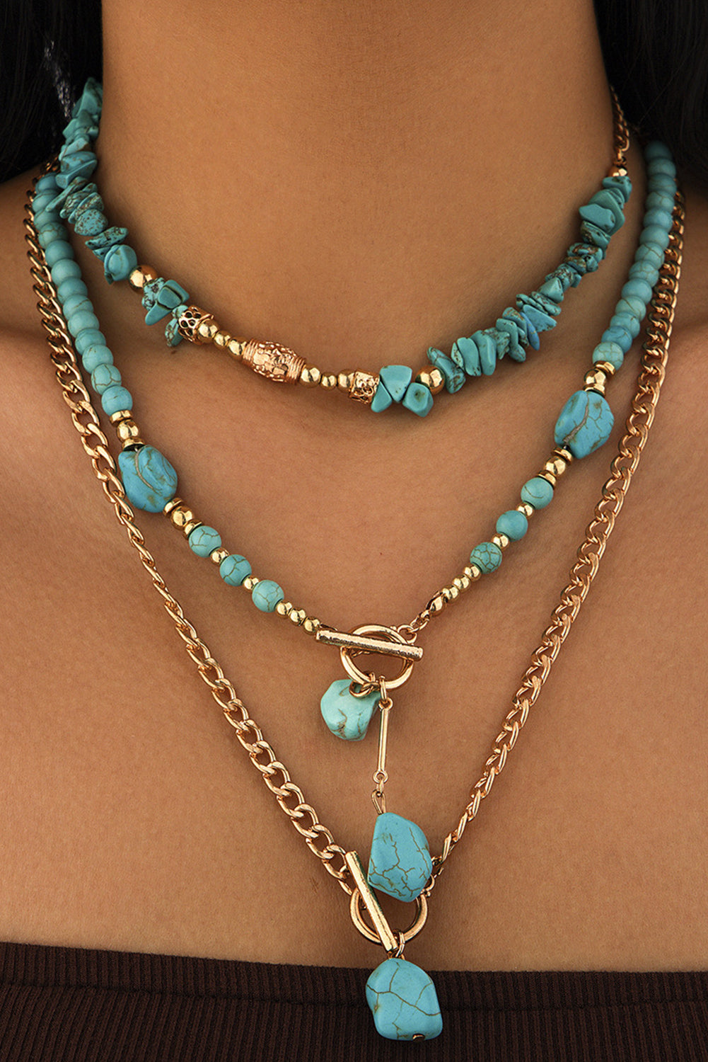 Layered necklaces with turquoise beads and gold chains on a person's neck.