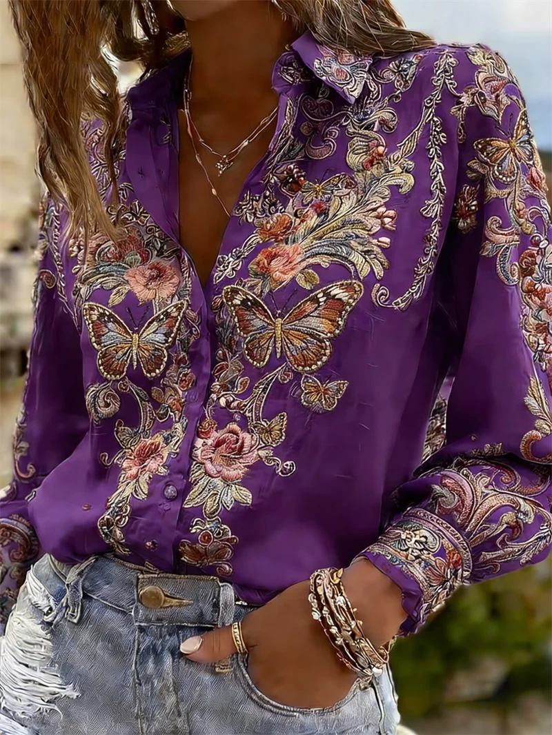 A close-up of a woman wearing a purple long-sleeve button-up shirt with intricate embroidered floral and butterfly patterns in gold, pink, and blue, paired with distressed denim shorts.