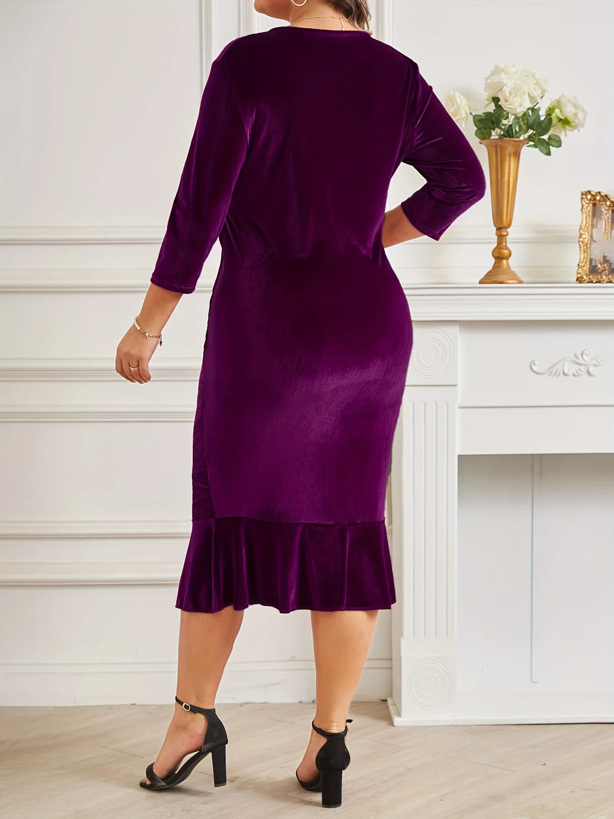 Woman wearing a purple dress with a ruffled hem in a room with white walls and a fireplace.