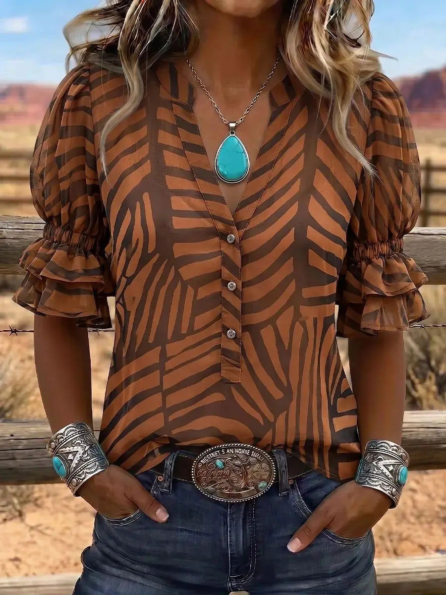 Person wearing a brown patterned blouse with ruffled sleeves, turquoise necklace, and belt buckle, standing against a desert landscape.