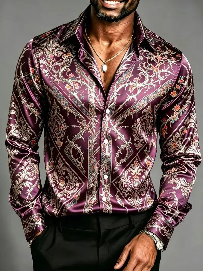 A man wearing a long-sleeve button-up shirt made of shiny purple satin with an ornate white, gold, and red paisley pattern, paired with black trousers.
