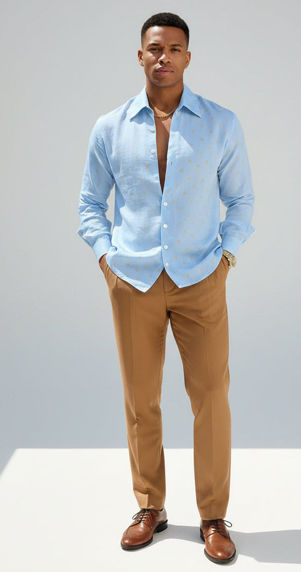 A man wearing a light blue long-sleeve button-up shirt with a small gold leaf pattern, paired with brown trousers.