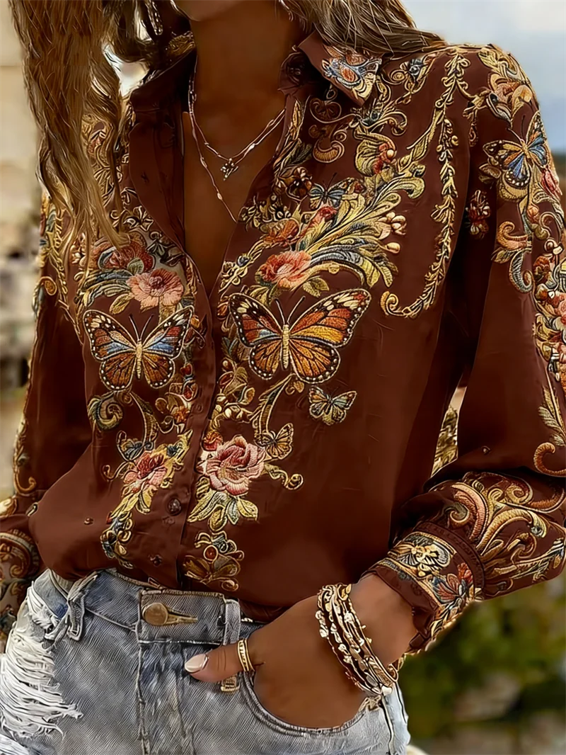 A woman wearing a brown long-sleeve button-up shirt with an intricate multicolor floral and butterfly print, paired with light-wash distressed denim jeans.