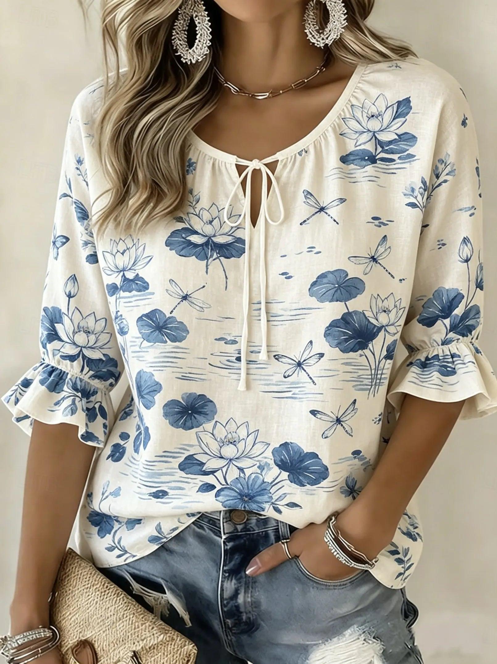 A woman wearing a cream-colored blouse with a blue lotus and dragonfly print, featuring a tie-neck detail and ruffled sleeves, paired with distressed denim jeans.