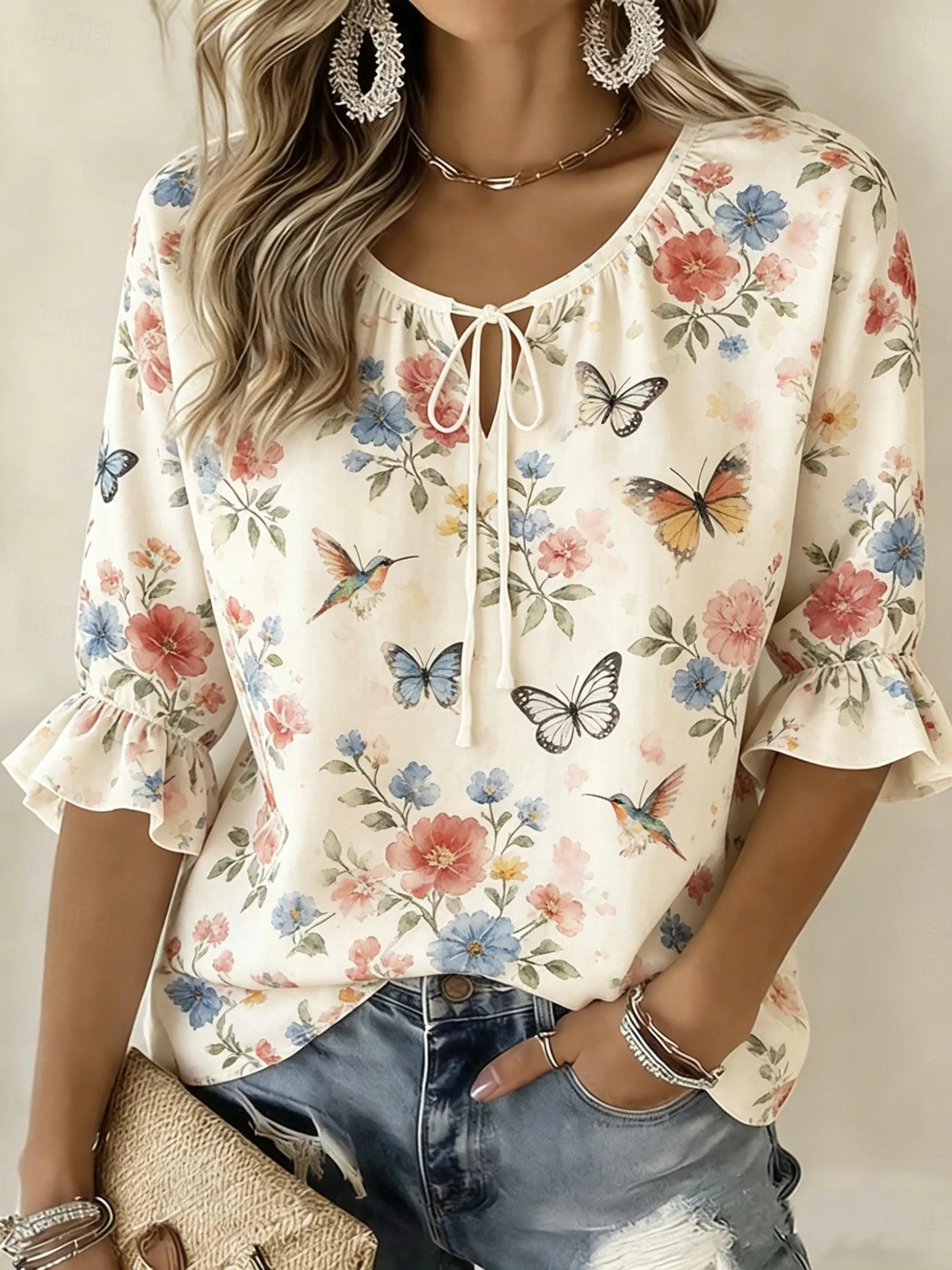 A woman wearing a cream-colored short-sleeve blouse with a ruffled tie neckline and a colorful butterfly and floral print, paired with distressed blue jeans.