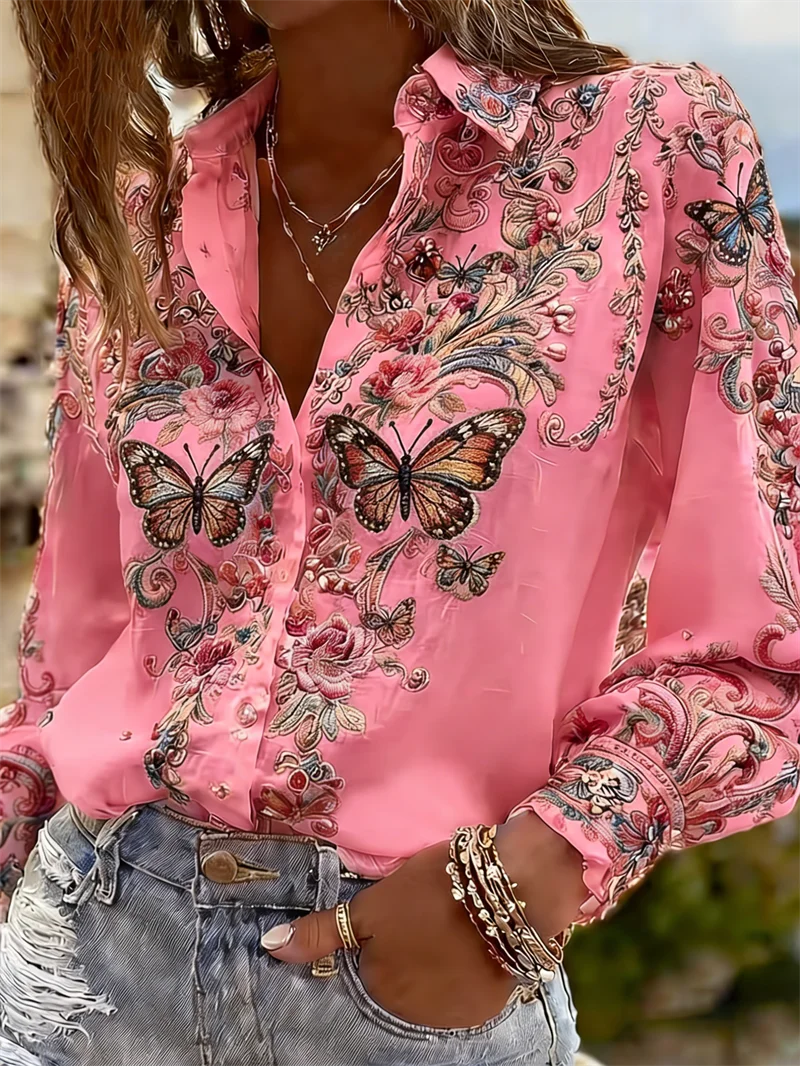 A close-up of a woman wearing a pink long-sleeve button-up blouse with ornate butterfly and floral embroidery , paired with light-wash distressed denim jeans.