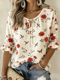 A woman wearing a cream-colored short-sleeve blouse with a red floral and bird print, paired with distressed blue jeans and silver jewelry.