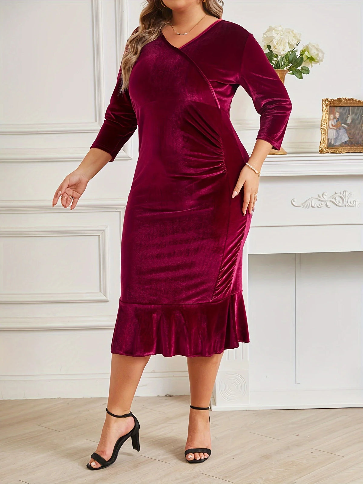 Woman wearing a burgundy velvet dress with a white fireplace and decorative items in the background