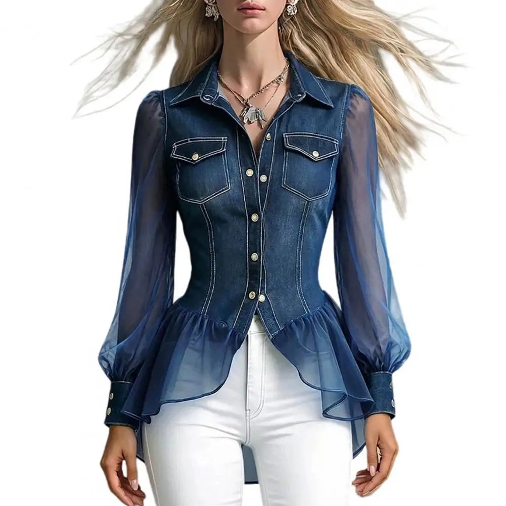 A woman wearing a fitted blue denim long-sleeve blouse with sheer mesh sleeves and a ruffled hem, paired with white pants, against a plain white background.
