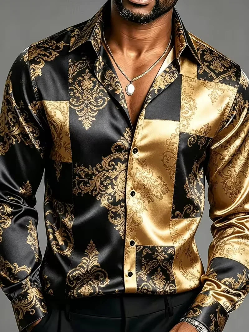 A close-up of a man wearing a long-sleeve satin button-up shirt with a black and gold damask patchwork pattern, paired with a silver pendant necklace.