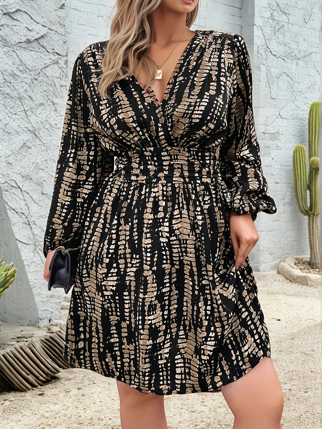 Woman wearing a black and gold patterned dress against a stone wall with a cactus.