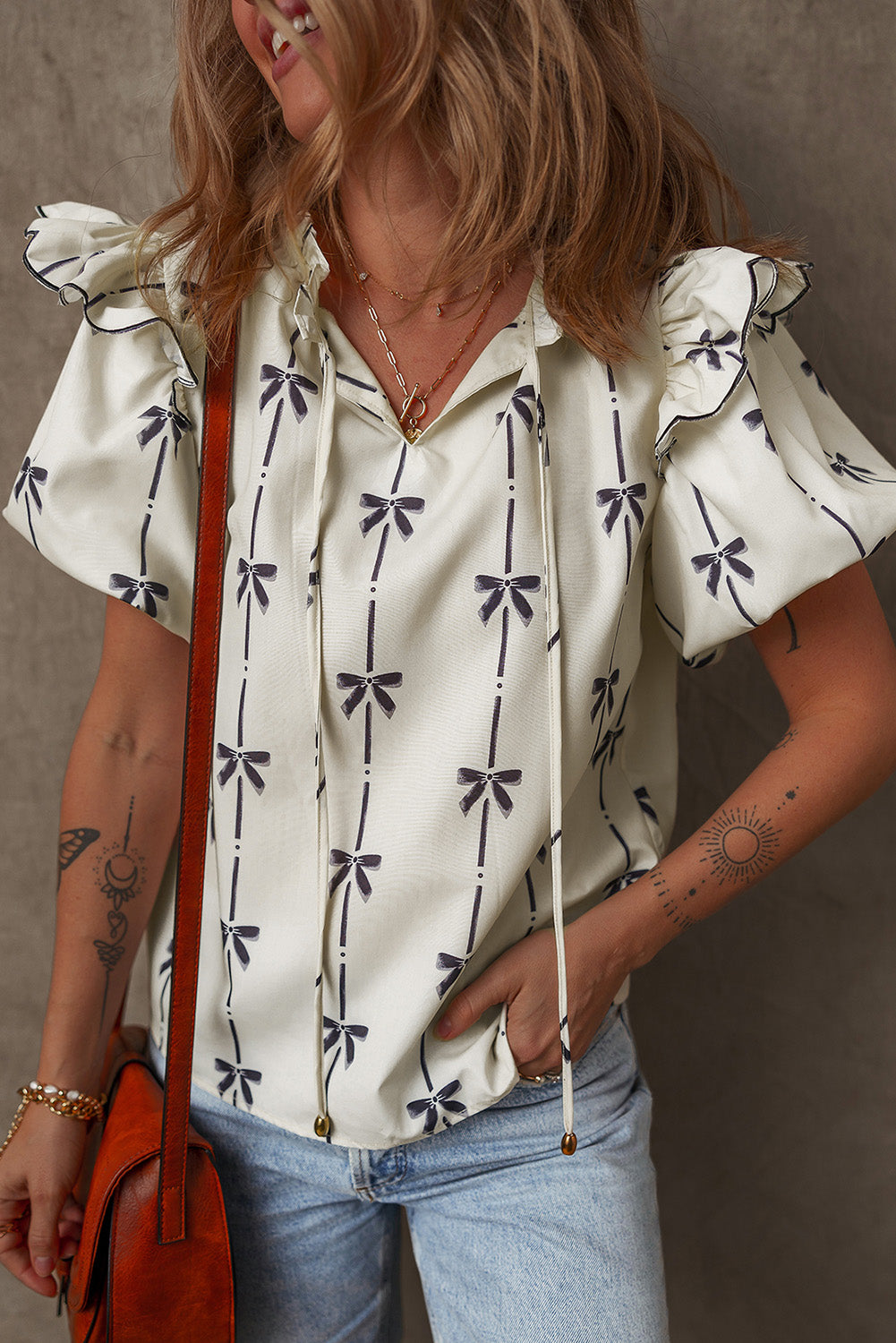 A woman wearing a beige short-sleeved blouse with a v-neck, featuring black bow prints and ruffled details.