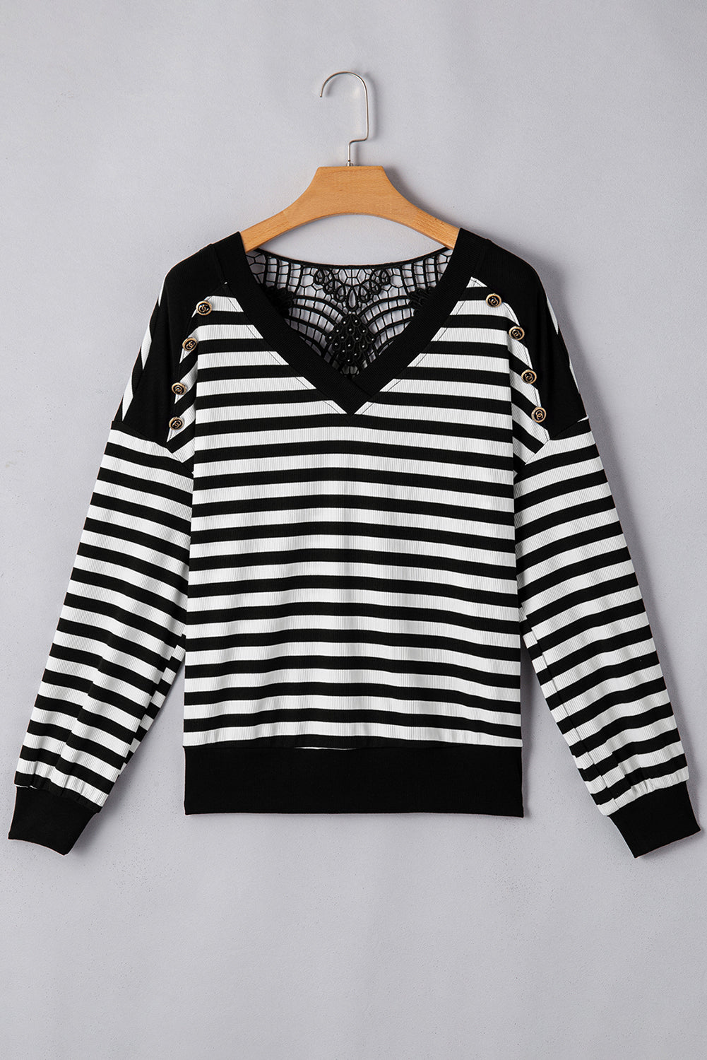 Black and white striped sweater with gold button decor on the shoulders and lace detail on the back on a hanger 