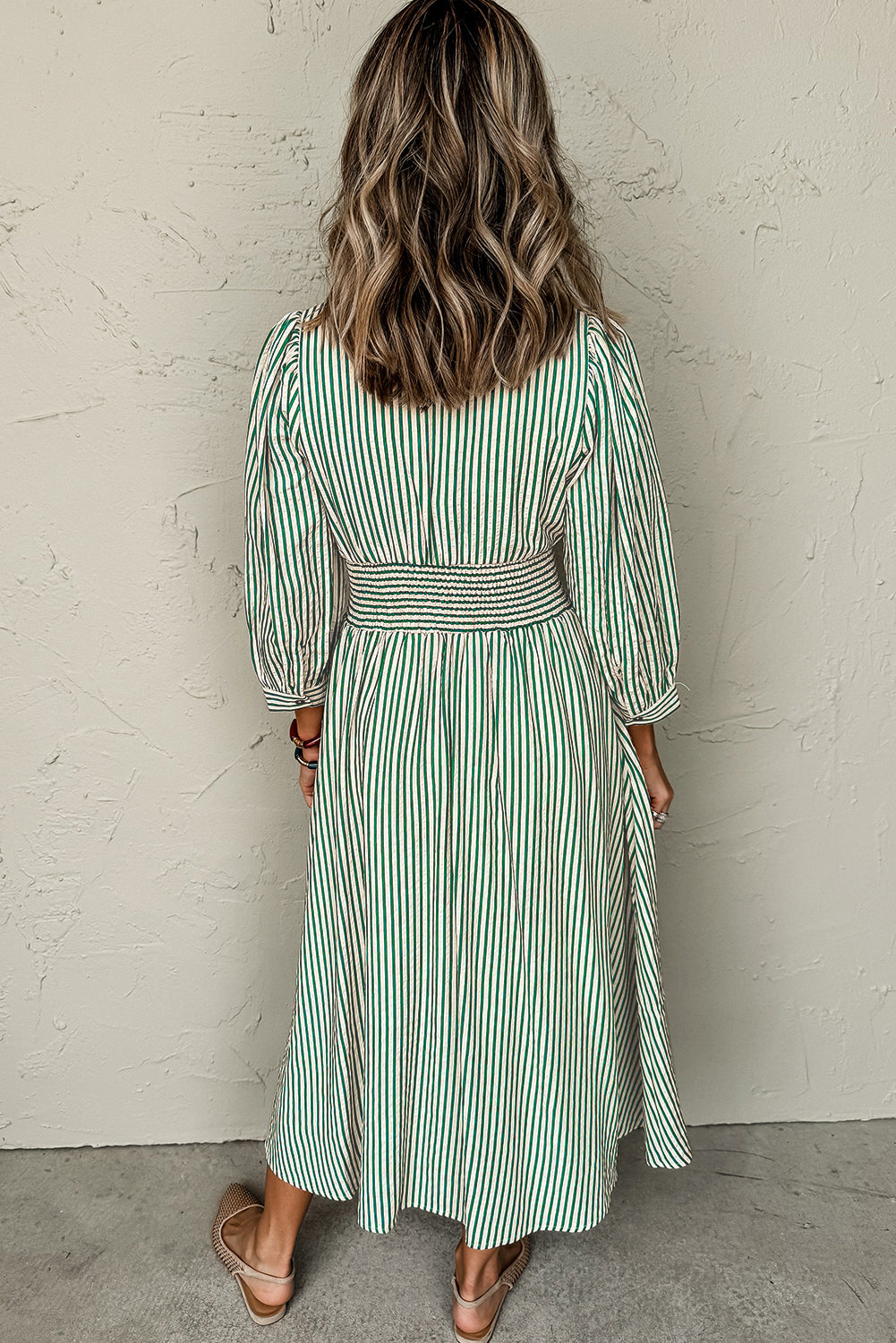 Woman wearing a green and white striped dress against a plain wall.